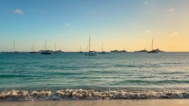 Karayipler Denizi manzarası. Adanın kumlu sahilinden uzakta demirli yelkenli tekneleri var. Gün batımında. Saint Martin Adası, Karayipler.