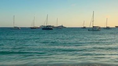 Karayipler Denizi manzarası. Adanın kumlu sahilinden uzakta demirli yelkenli tekneleri var. Gün batımında. Saint Martin Adası, Karayipler.