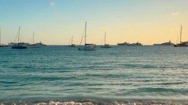 Karayipler Denizi manzarası. Adanın kumlu sahilinden uzakta demirli yelkenli tekneleri var. Gün batımında. Saint Martin Adası, Karayipler.