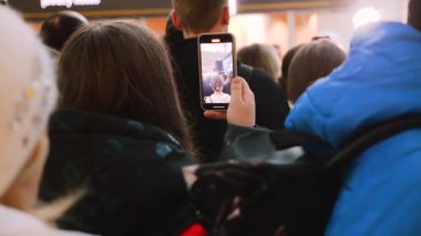Genç hayranlar bir alışveriş merkezinin avlusunda akıllı telefonlardan konser çekiyorlar. Büyük bir gençlik kalabalığı sahnenin yanında toplandı. Enerji dolu izleyiciler halka açık bir etkinlikte konser veriyor..