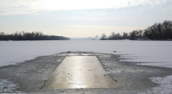 Прямоугольная ледяная дыра на реке для купания и закалки тела. Морозное зимнее время с пушистым снегом.