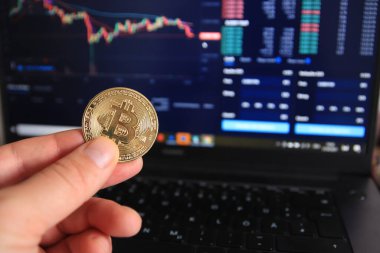 Adamın elinde Bitcoin BTC 'nin fiziksel versiyonu var. Arkaplanda borsada analiz edilen veriler var.