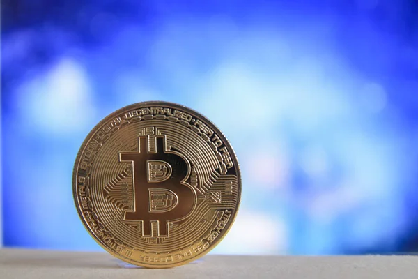 Bulanık mavi arkaplanı olan Bitcoin BTC 'nin fiziksel bir versiyonu.