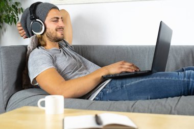 Evde dizüstü bilgisayar kullanan ve cep telefonuyla konuşan yakışıklı, beyaz bir adam.