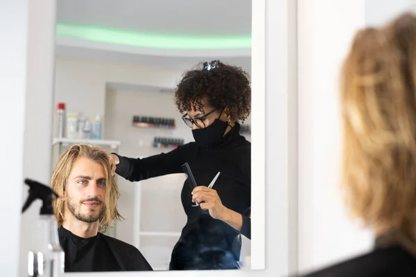 Positive young Black hairdresser enjoying working in beauty salon and blowdrying hair of client