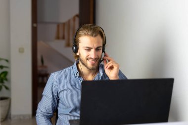 Evde kulaklıkla çalışan sarışın bir erkek dizüstü bilgisayarda kablosuz internet kullanıyor, erkek çağrı merkezi temsilcisi ya da tele pazarlamacı.