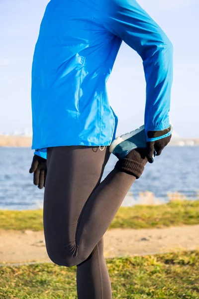 Woman stretches legs before cardio workout outdoors in autumn park in warm clothes.