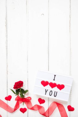 Sevgililer günü, aşk, romantik konsept. Kurdeleli taze kırmızı gül çiçeği ve beyaz ahşap arka planda ışık kutusunda seni seviyorum mesajı. Tebrik kartı. Düz konum, üst görünüm, kopyalama alanı.