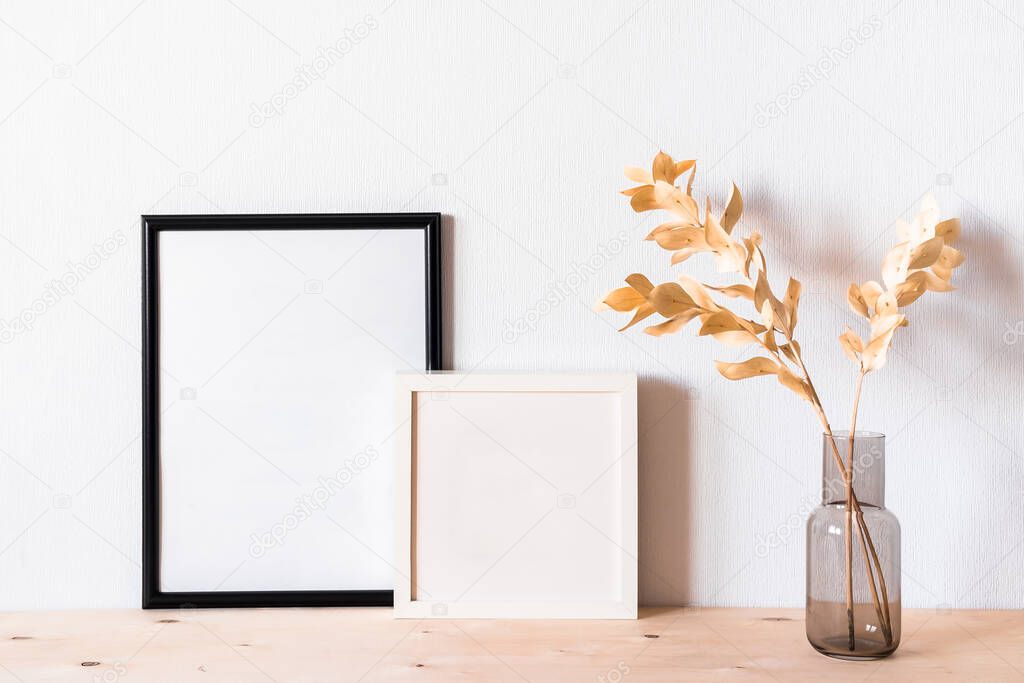 Dried flowers and a photoframes against a light wall in a minimalist style