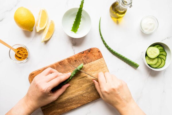 Homemade skin care concept. Female hands making a cosmetic mask from natural ingredients aloe vera, lemon, yogurt, turmeric, olive oil, cucumber on a light background