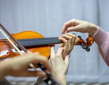 Keman çalarken çocukların ellerini yerleştirerek öğretmene elini doğru şekilde tutmasında yardımcı oluyor.
