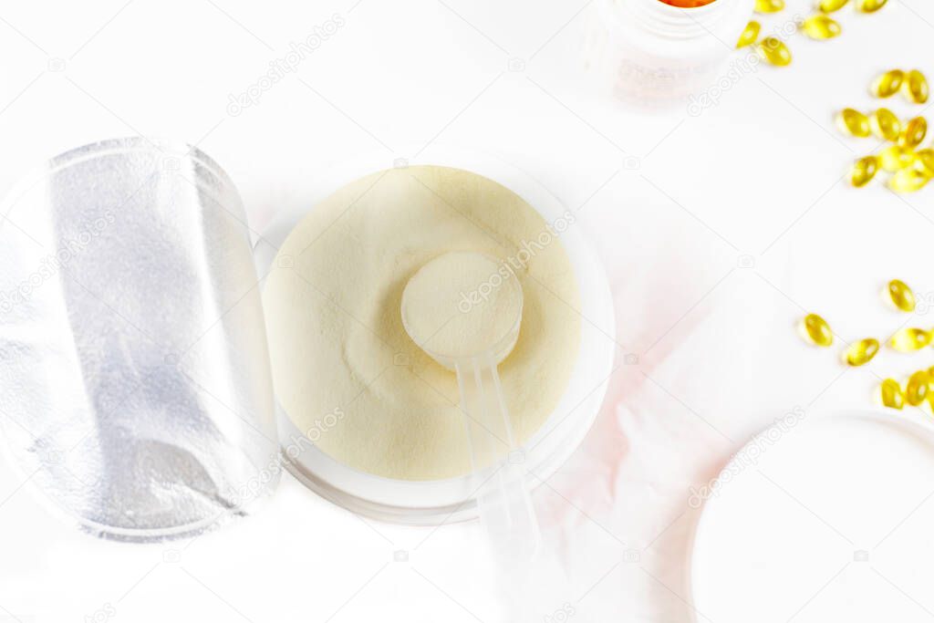 cologen powder for face rejuvenation in a serving spoon with vitamin D capsules on a white background