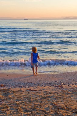 Kumsaldaki küçük çocuk gün batımında denize gider. 
