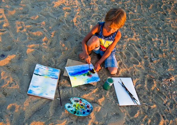 little squatting artist paints a landscape on the seashore in the evening