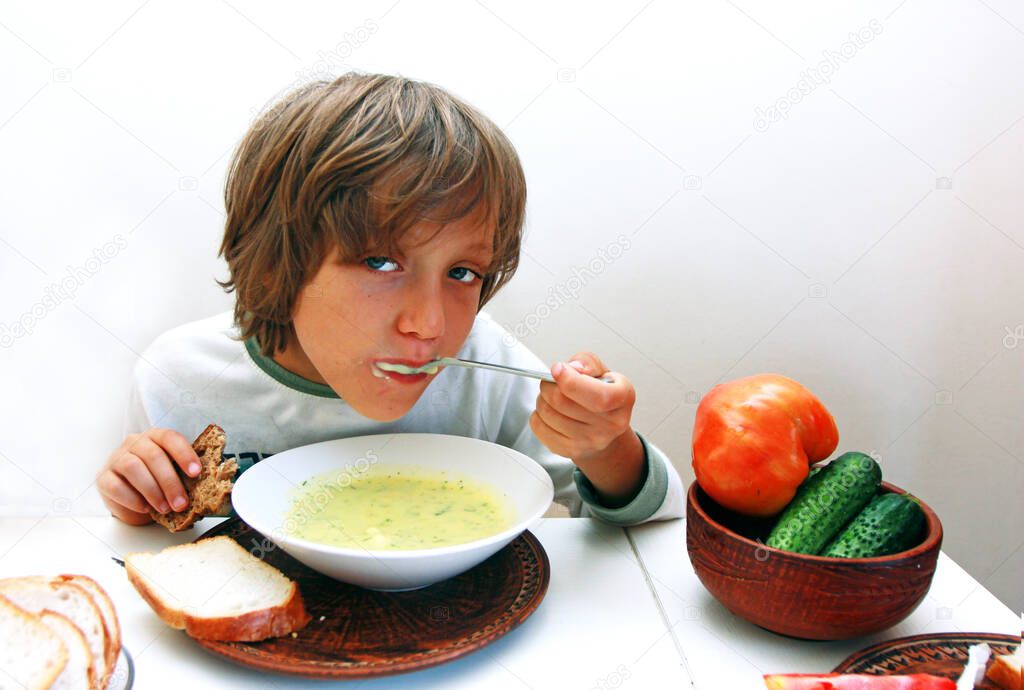 boy eats vegetable soup with spoon and bread at the dinner table