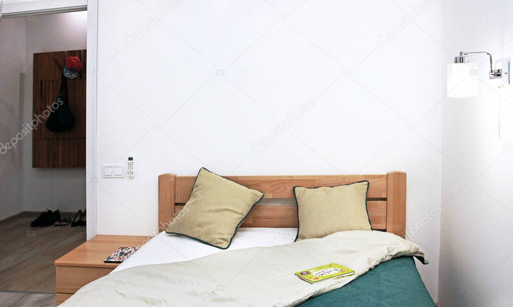 cozy pan-bedroom interior with a green bedspread, two pillows, a luminous sconce, a book on the bedspread with a door to the hallway