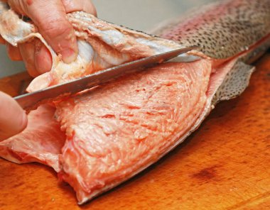 Şef, ahşap bir tahtanın üzerindeki kırmızı balığın derisini yüzer. Suşi hazırlar, yatay, arka plan, bulanık.