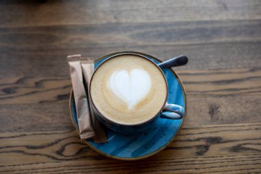 Masanın üzerinde kalp şeklinde köpüklü kahve ve şeker dolu bir çanta.