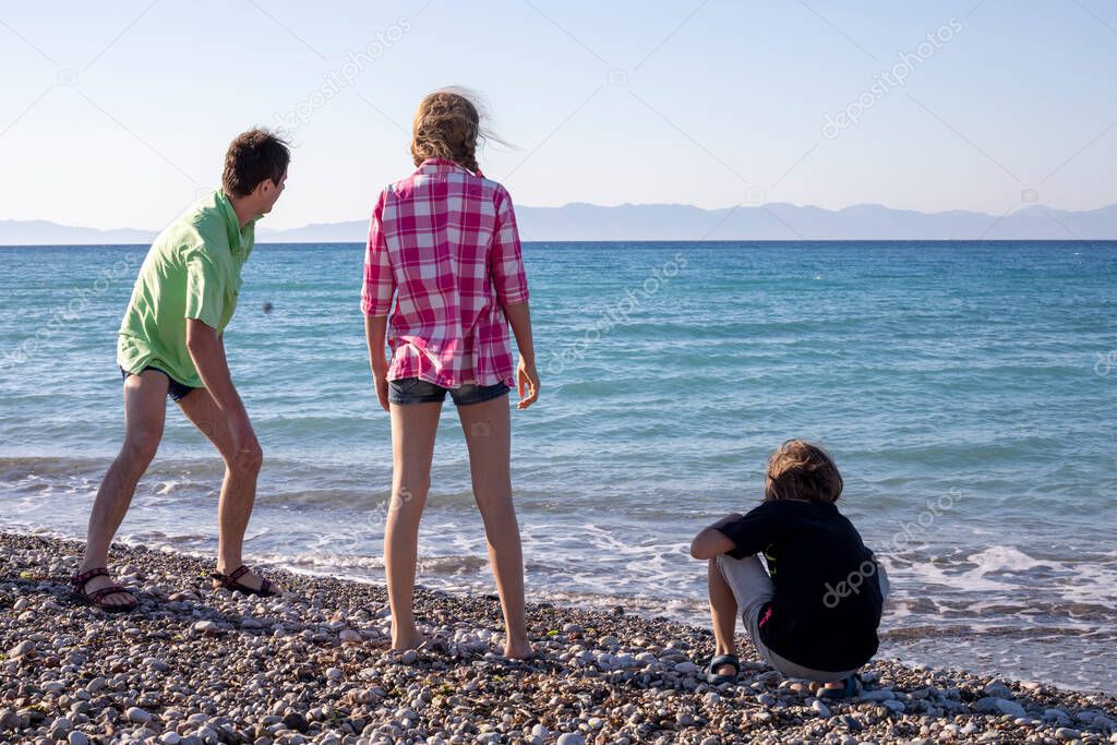 happy dad shows children how to throw stones into the sea, family vacation, Greece