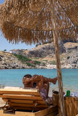Yunanistan 'ın Rodos kentindeki St. Paul körfezinde bir şemsiye altında sahilde mutlu bir adam.