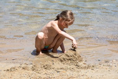 Mutlu küçük kız deniz kenarında kumla oynuyor, ufuk.