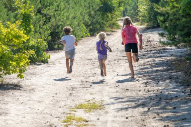 Mutlu çocuklar güneşli bir günde ormanda yalınayak koşarlar, Ufuk.