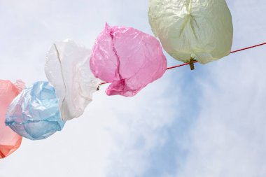 Tek kullanımlık renkli torbalar, bulutlar ve çevrenin plastik kirliliğine karşı yeniden kullanılmak üzere bir iple kurutuluyor.