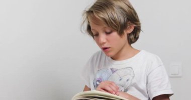 Çalışkan çocuk masa başında beyaz bir duvara karşı ilginç bir kitap okuyor, okula geri dönüyor, özgün.