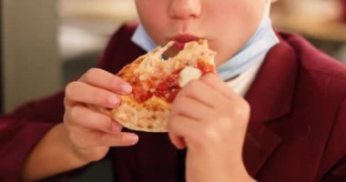 Pandmi molasında pizza yiyen mutlu okul çocuğu.