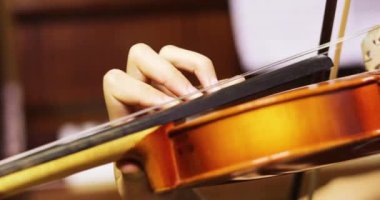 Kemancı kemanla müzik çalar. Sırtı piyanonun yanında, yatay.