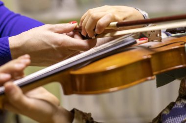 Hocanın eli, keman çalarken boynunu tutan genç kemancının sağ elini doğrultuyor, goizontal.