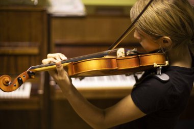Genç kemancı, sırtı piyanonun yanında yatay olarak kemanla müzik çalar.