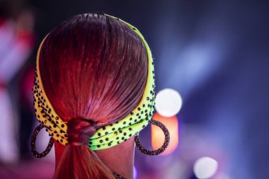 Latin bir programda kadın bir dansçının taktığı yuvarlak küpeli açık yeşil saç bandı.