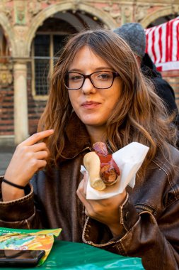 Mutlu genç kız tatil fuarında Alman sosisi yemekten hoşlanıyor..