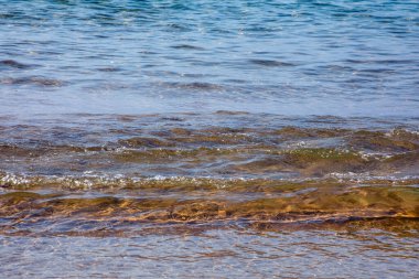 Kumlu bir sahilden dalgalarla dolu sakin bir deniz manzarası. Deniz kenarı tatili