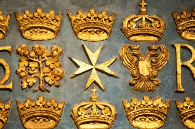 Oyulmuş altın semboller, altın taçlar ve dokulu bir panele Malta haçı.