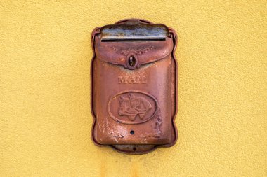Dışarıdaki sarı duvarda dövülmüş metal bir posta kutusu var.