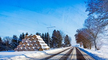 Güneşli bir günde karla kaplı kütüklerle dolu kalabalık bir bölgede karla kaplı bir yol.