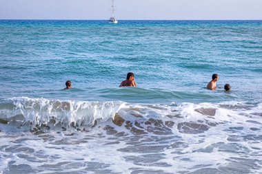 Bir aile deniz dalgalarında bir yelkenlinin arka planına karşı yüzer. Aile tatili