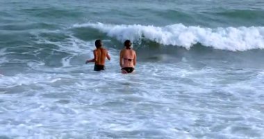 Mutlu çocuklar kıyıdan büyük dalgalara atlarlar. Denizde okul tatili