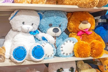 Oyuncak dükkanında rafta duran büyük yumuşak beyaz, kahverengi ve mavi oyuncak ayılar.
