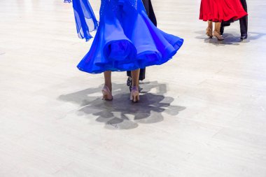 Dans eden bir çift mavi elbise ve siyah palto ve kırmızı elbise ve siyah palto ile standart bir dans gösterisi yapar.