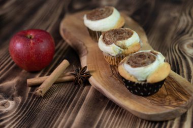 Tahta bir tahtanın üzerinde ev yapımı tarçınlı kekler ve desenli kahverengi masa kompozisyonunda kırmızı elma.