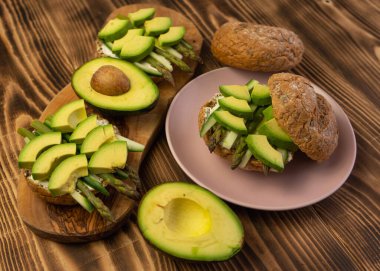 Sağlıklı vejetaryen organik kahvaltı sandviçi kuşkonmaz, avokado, salatalık, tam tahıllı çöreğin üzerine yumuşak peynir. Tahta, tahtayı kapat.