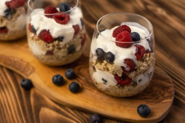 Sağlıklı vejetaryen kahvaltı tatlıları yulaf, süt, yoğurt, bal, yağ tulumu, ahududu ve tam tahıllı camdan yapılır. Tahta, tahtayı kapat.