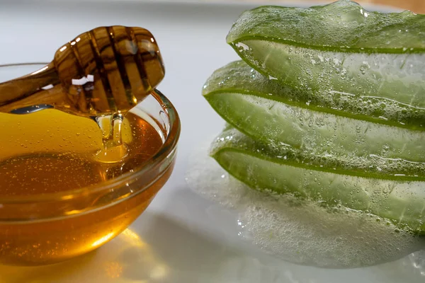 Aloe Vera slices with juice and honey wood spoon on white plate, skin care spa — Stock Photo, Image