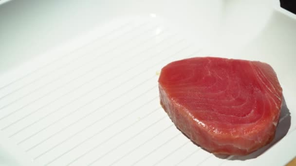 Mano femenina dejando filete de atún crudo para freír en una sartén blanca acanalada, 4K de cerca — Vídeo de stock
