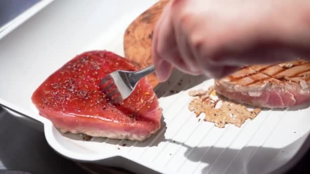 Handen omdraaien tonijn steak geribbelde witte pan met vork en keuken houten spatel — Stockvideo