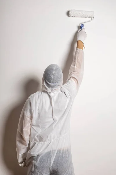 man with paint roller dressed in white protective suit