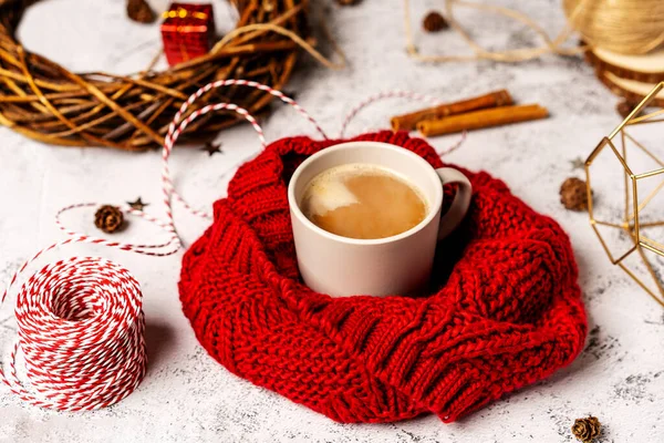 Coffee mug in a soft red winter scarf on a gray background with Christmas decorations. Christmas coffee break for home recreation. The view from the top